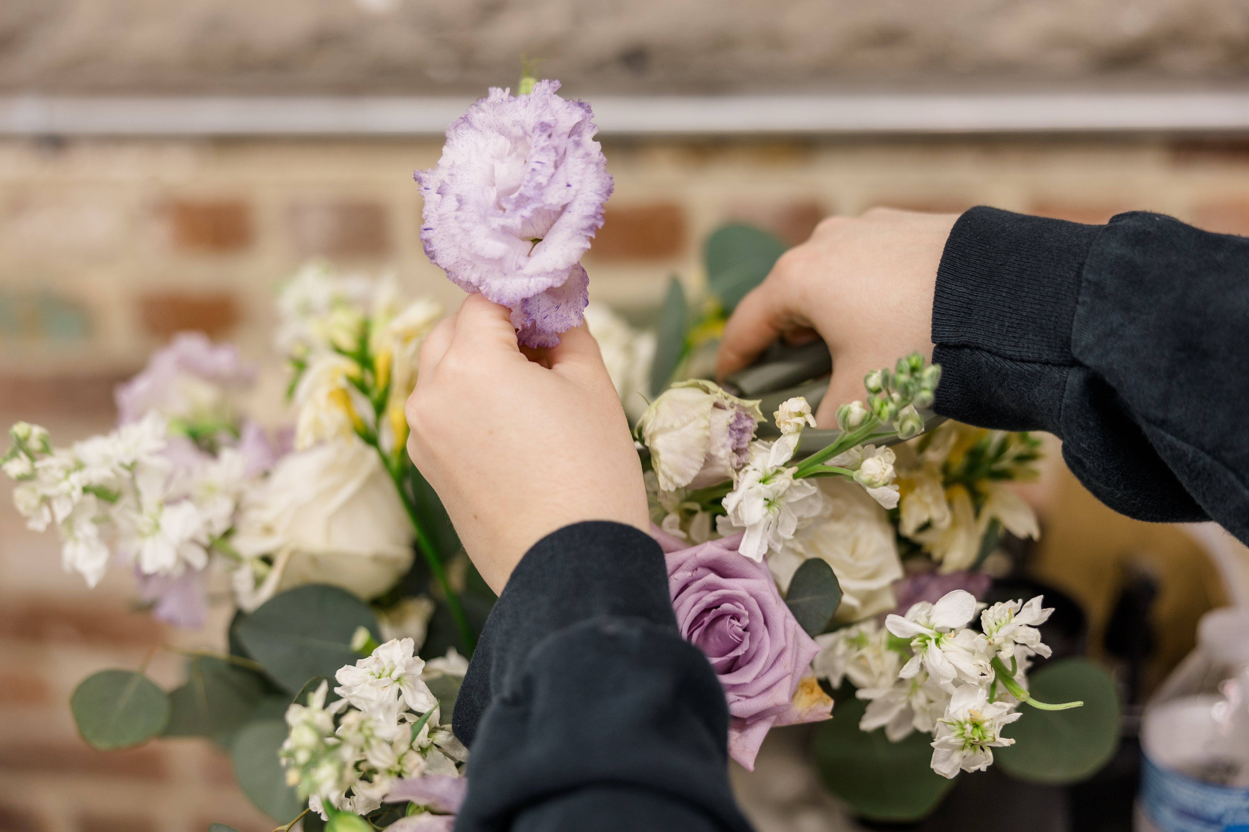 A hand holding onto a fresh purple bloom from a large wedding bouquet.