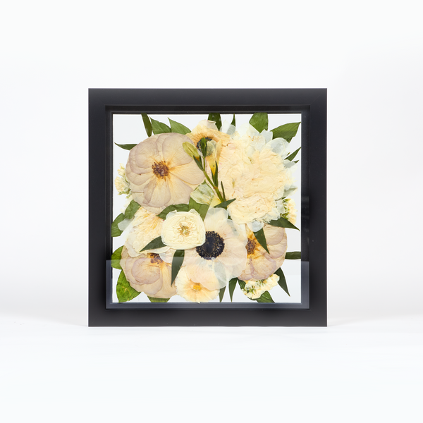 Wedding bouquet preservation frame in a 10x10 size with black wood surround. All white and green pressed florals with pressed quicksand roses displayed in our burst design style. 