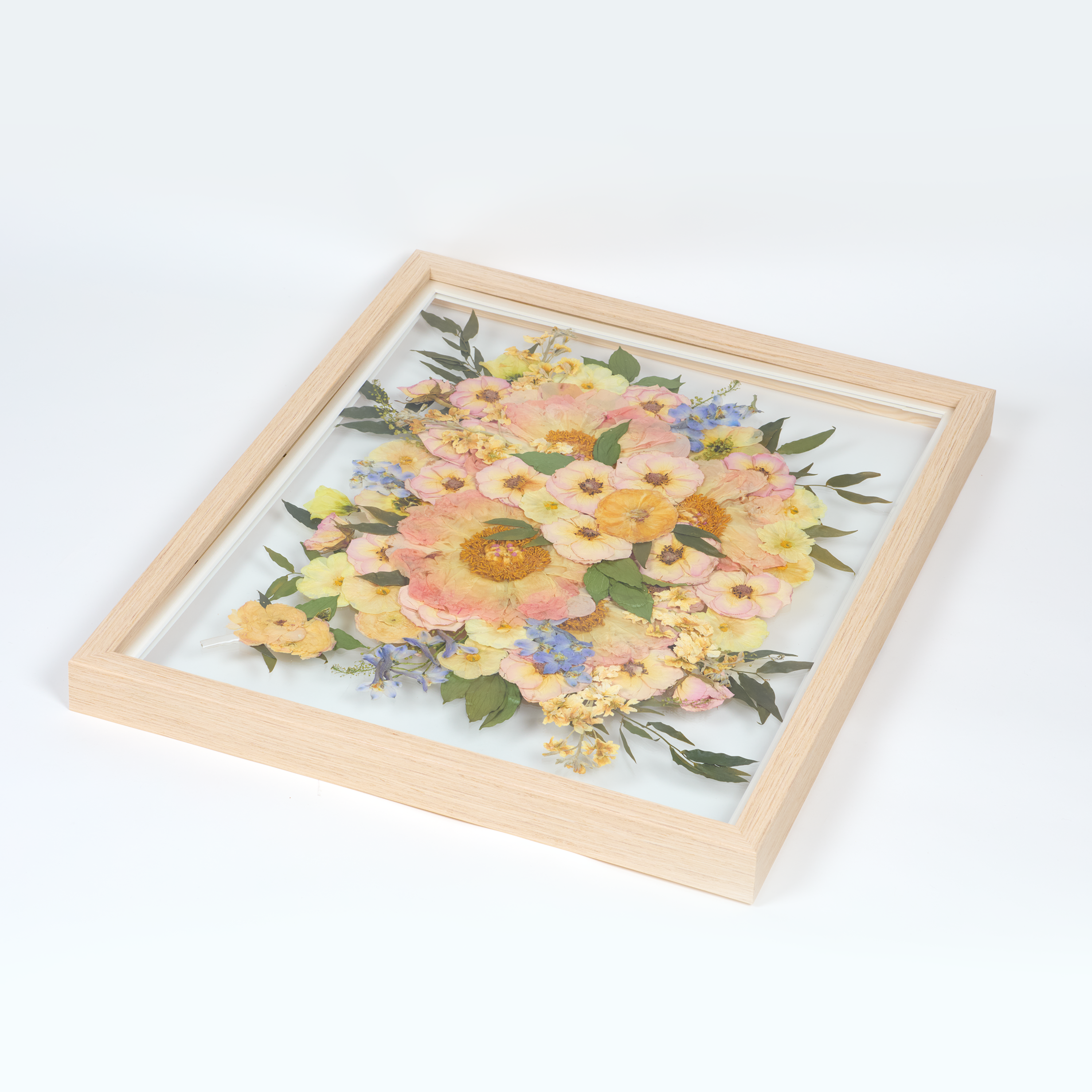 Bridal bouquet preservation in a 16x20 natural wood frame. Pink, coral, and blue pressed florals fill the frame with a floating glass background. 
