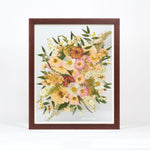 A large pressed floral bouquet encased in a brown frame with a date written in white script