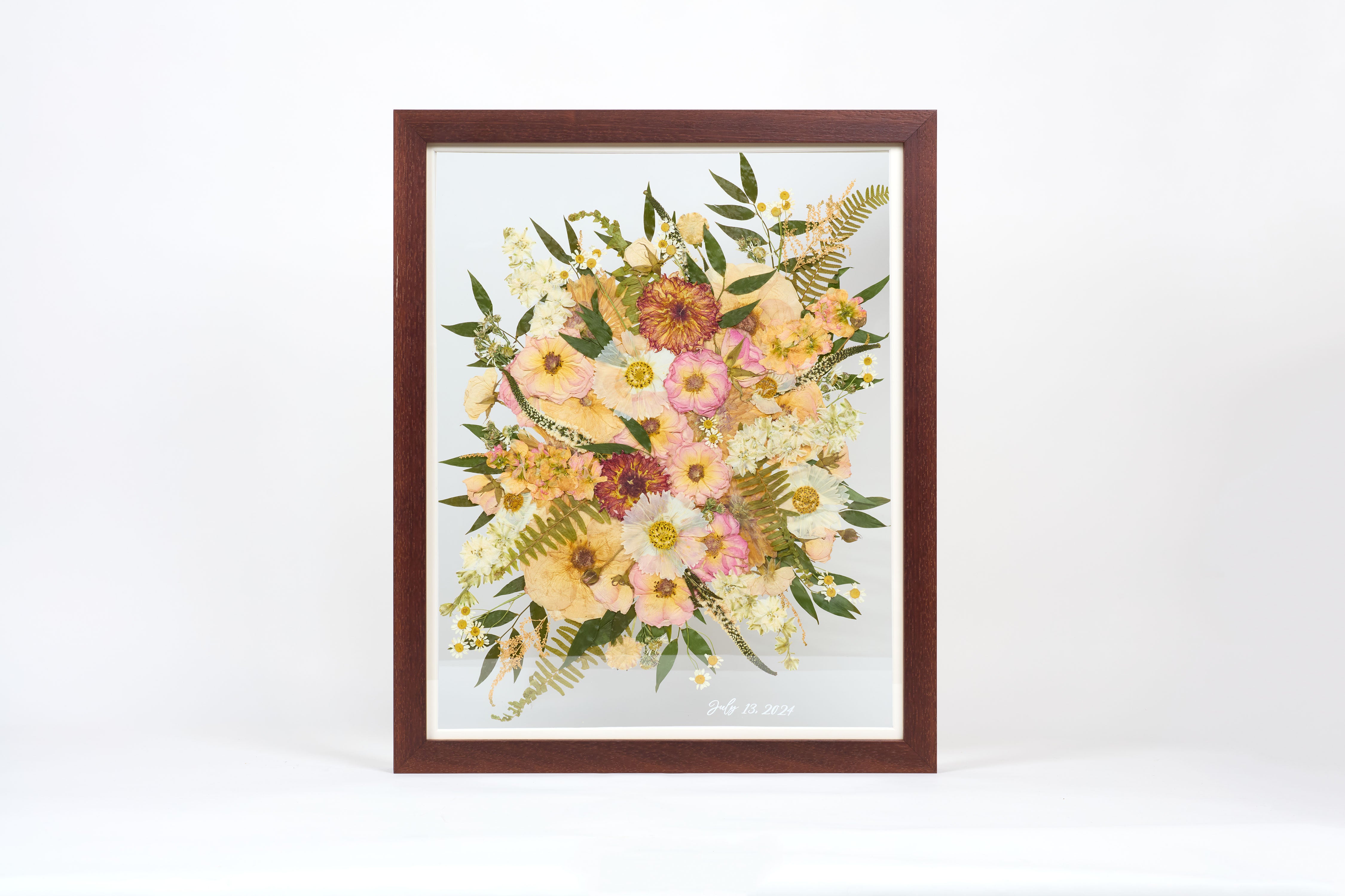 A large pressed floral bouquet encased in a brown frame with a date written in white script