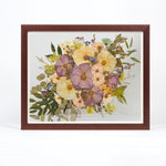 A large horizontal brown frame with pressed colorful roses and greenery