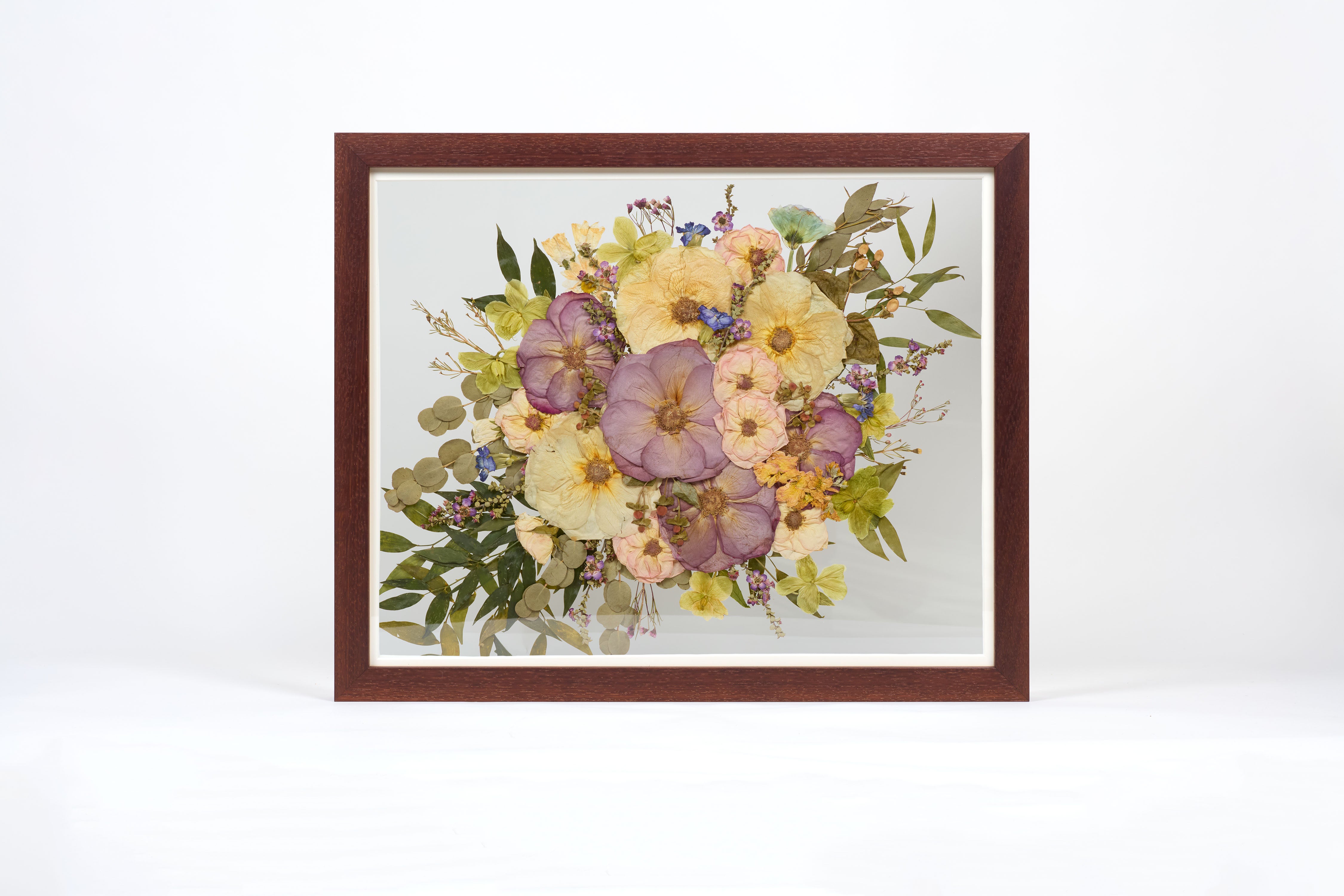 A large horizontal brown frame with pressed colorful roses and greenery