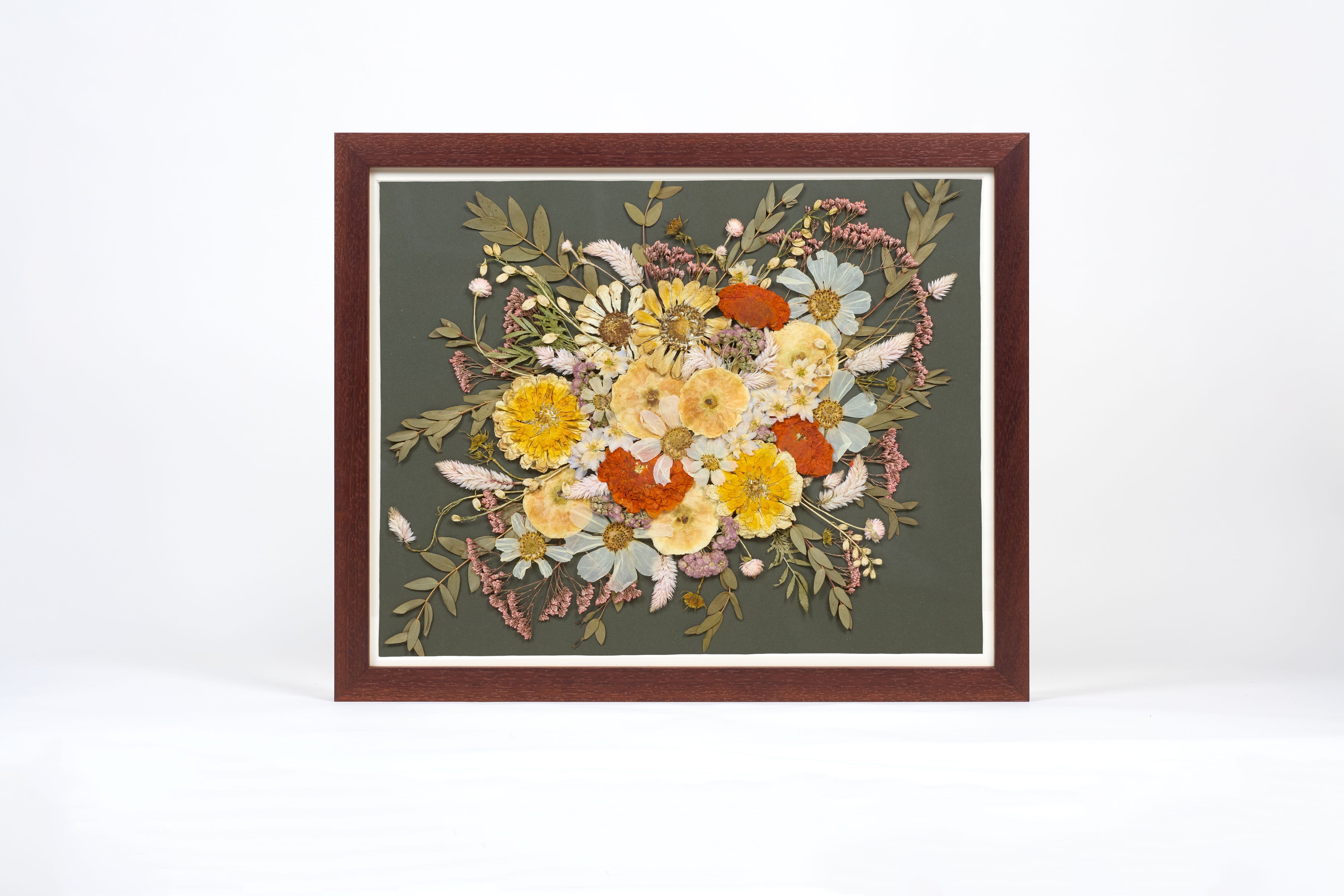 A walnut wood frame with preserved flowers encased on top of a dark green background