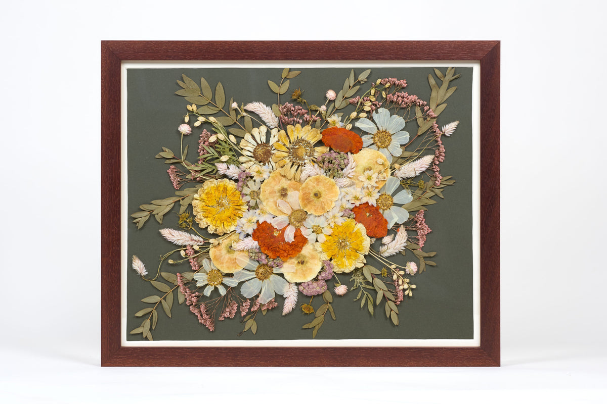 A walnut wood frame with preserved flowers encased on top of a dark green background