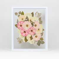 A pressed bridal bouquet in a white wood floating frame featuring pressed pink and white florals. 