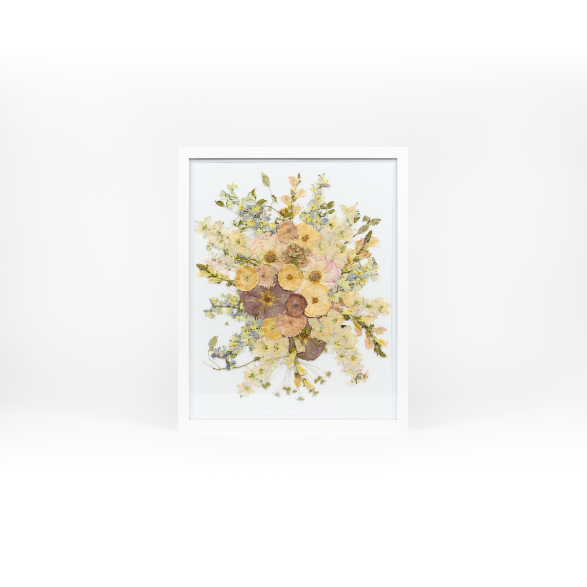 A pressed bridal bouquet in a white wood frame with an archival white background featuring pressed garden blooms such as roses, delphinium, and ranunculus. 