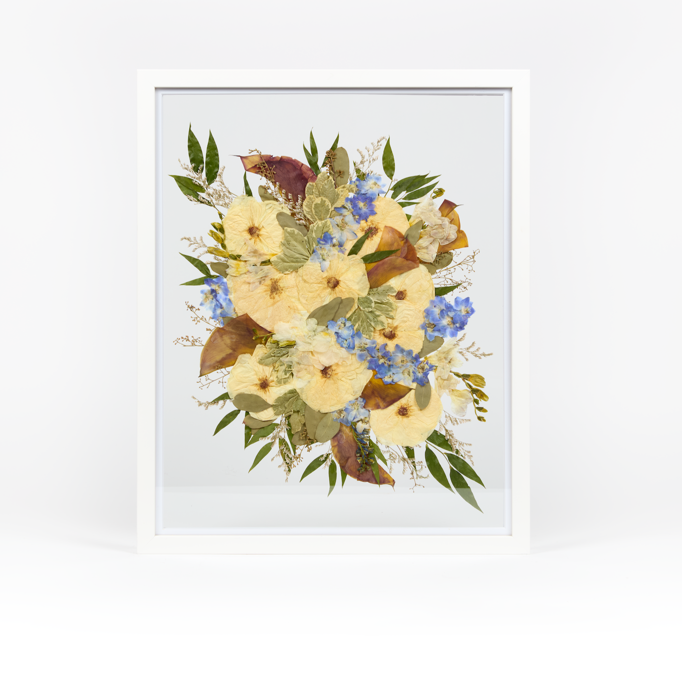 A pressed bridal bouquet in a white wood floating frame featuring pressed roses, delphinium, and calla lilies. 