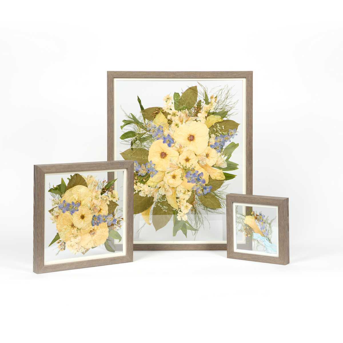 A wedding bouquet preservation set with three frame sizes and barn wood moulding. The flowers are white, blue, and green pressed florals. 