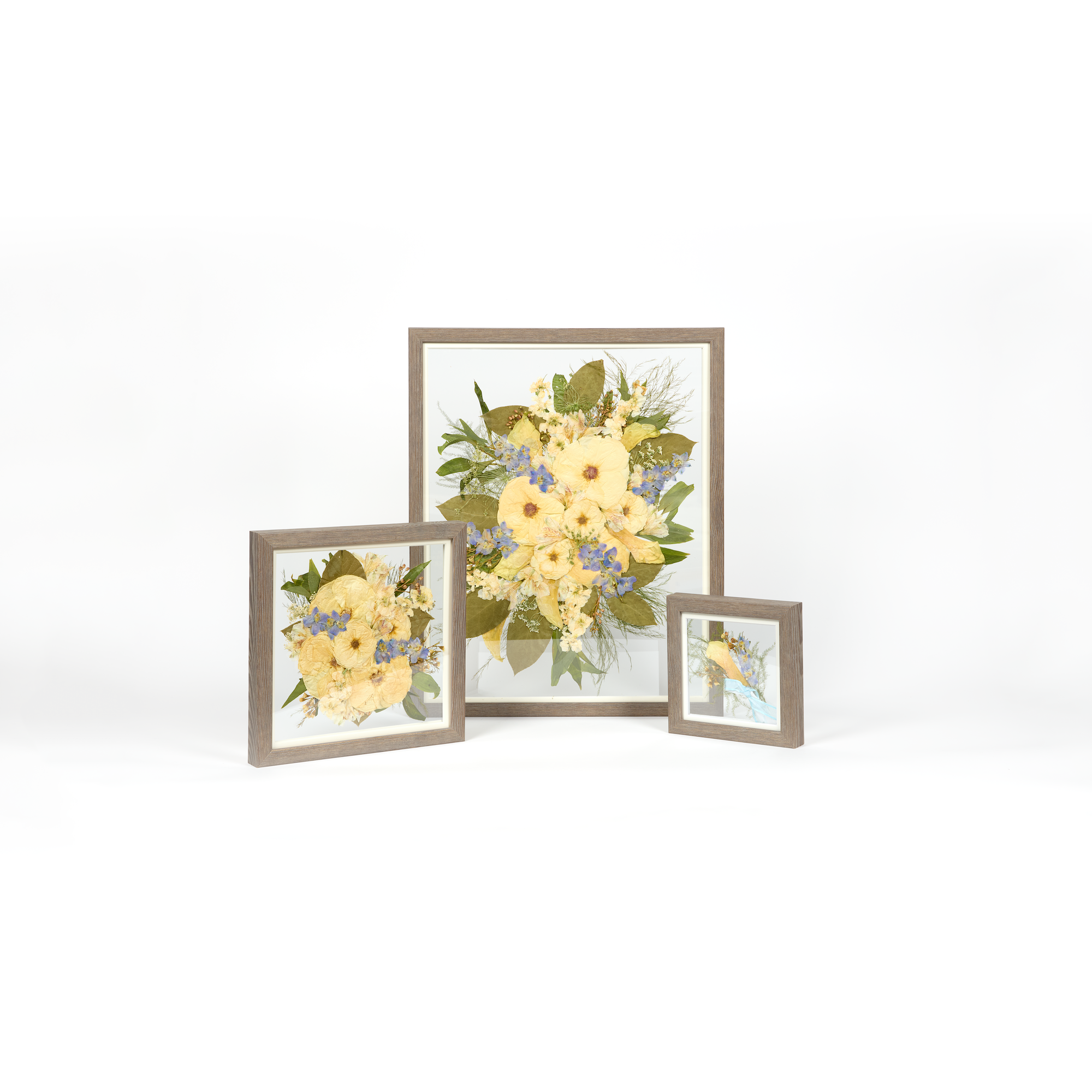 A wedding bouquet preservation set with three frame sizes and barn wood moulding. The flowers are white, blue, and green pressed florals. 