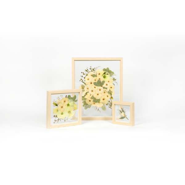 An all white and green wedding bouquet preservation set with three different sized frames in the natural wood surround.