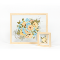 A wedding bouquet preservation frame set with white and blue pressed florals and pressed greenery.  