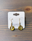 A pair of gold dangle earrings feature real pressed white flowers in a circular gold bezel setting. They are set against a wooden background in a white earring holder.