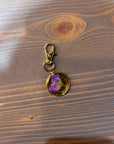 A gold pressed flower keychain includes one small purple flower. It is placed against a wooden background. 