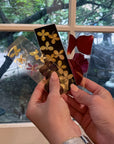 Three pressed flower bookmarks being held against a window