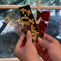 Three pressed flower bookmarks being held against a window