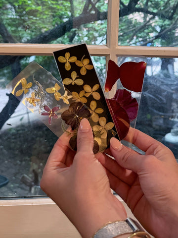 Three pressed flower bookmarks being held against a window