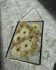 a large pressed flower gold hanging frame against a white rug.