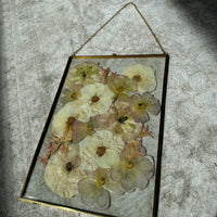 a large pressed flower gold hanging frame against a white rug.