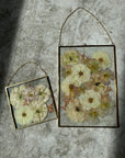 a small and big gold hanging frame encased with pressed flowers in a beautiful burst design against a white rug.