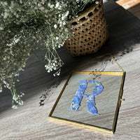 square gold hanging frame with blue pressed flowers. 