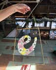 a big gold ganging frame designed with springy blooms in the shape of the letter e being held by someone.