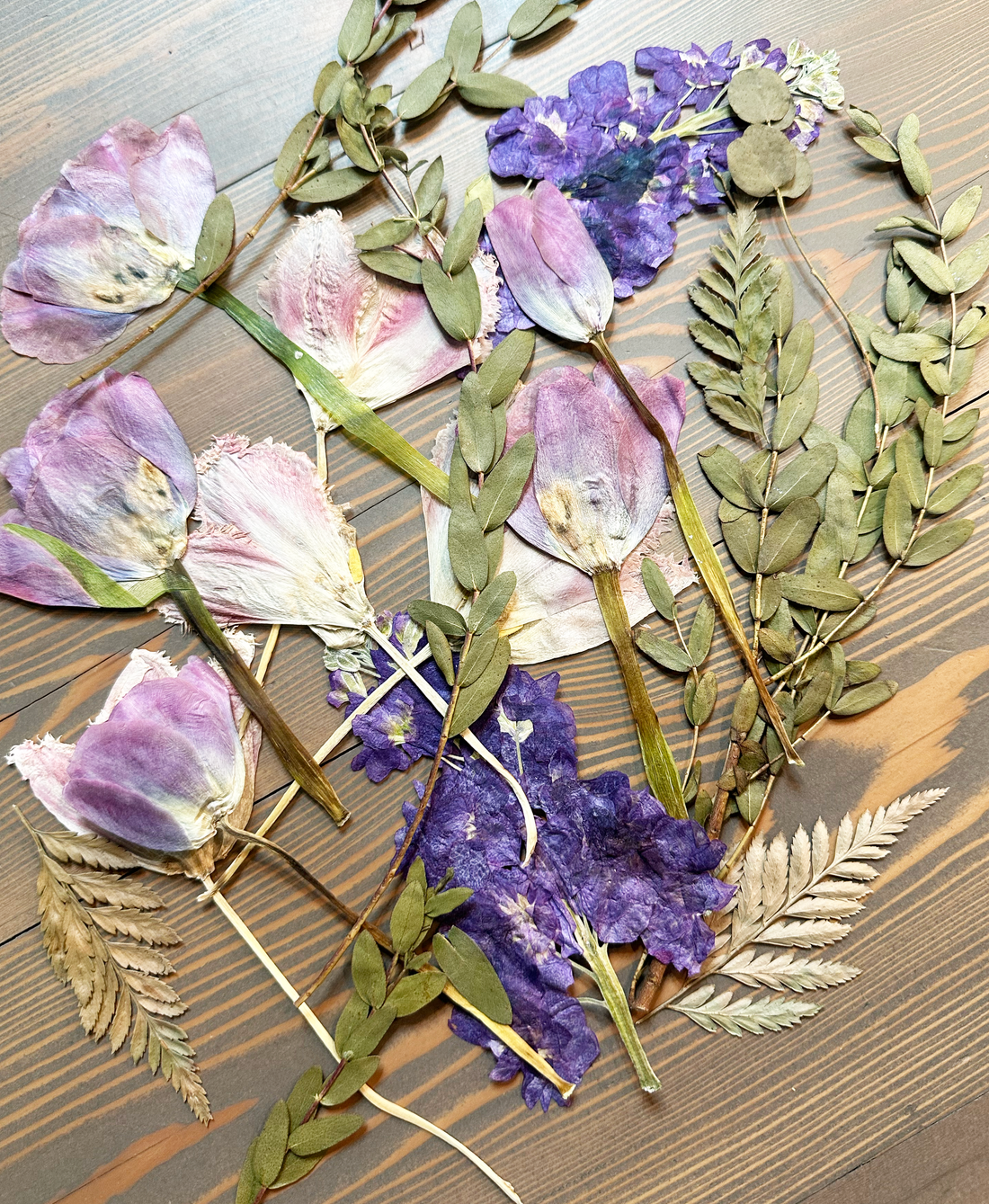 Purple pressed flowers and greenery against a wooden table.