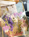 gold hanging frame with purple pressed florals being held by a person that designed it at a workshop.