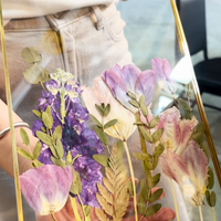 gold hanging frame with purple pressed florals being held by a person that designed it at a workshop.