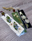 Three bookmarks on a wooden table with pressed flowers and attached by a string and beads