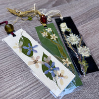 Three bookmarks on a wooden table with pressed flowers and attached by a string and beads