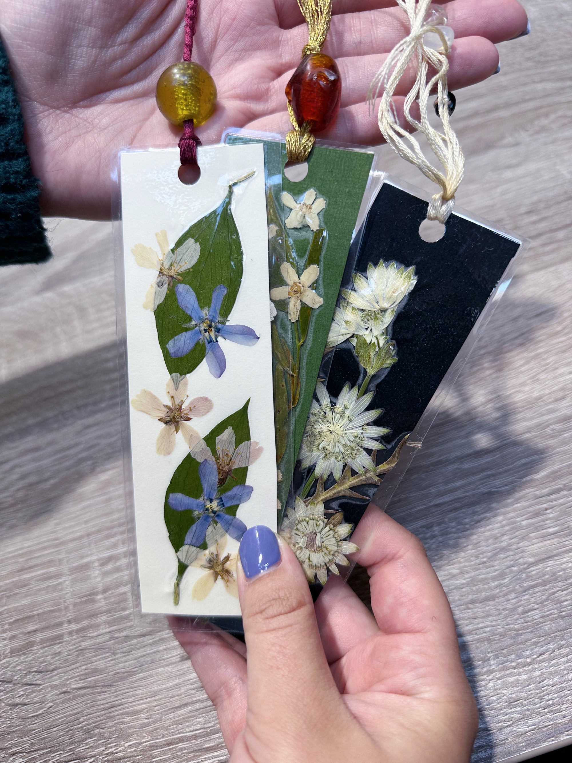 Hands holding three bookmarks that have preserved flowers inside