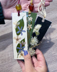 Hands holding three bookmarks that have preserved flowers inside