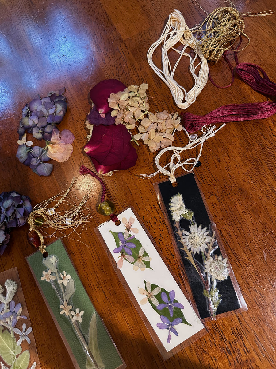 A wooden table that has string, pressed flowers, and bookmarks on top