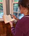 A woman reading a book holding a pressed flower bookmark to hold open the page