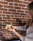 a woman holding a small white pumpkin designed with pressed florals in front of a brick wall