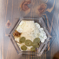 A hexagon resin ring dish with pressed white flowers and greenery set against a wooden surface. 