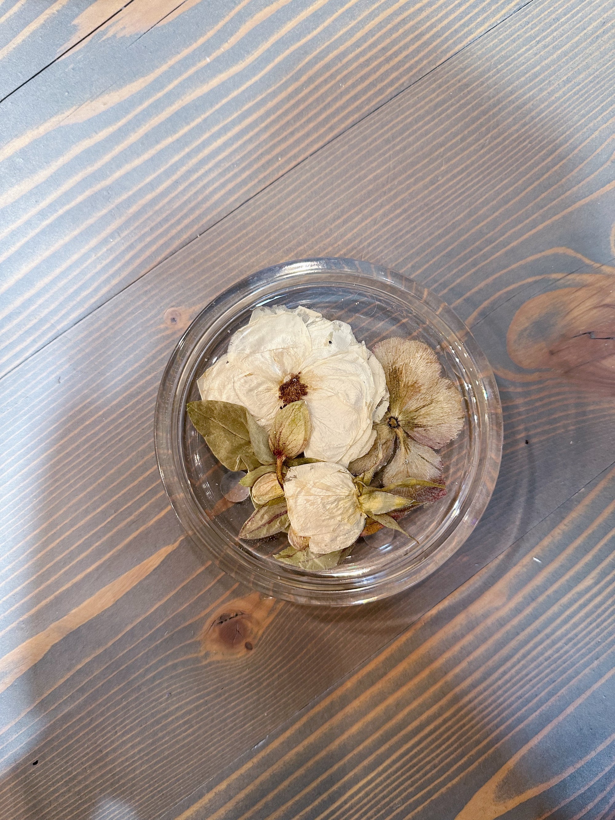 A circular resin ring dish with pressed white flowers is set atop a wooden surface. 