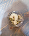 A circular resin ring dish with pressed white flowers is set atop a wooden surface. 