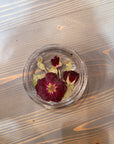 A circle resin ring dish with a pressed red rose, two spray roses, and a few green leaves is set on top of a wooden surface. 