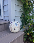 a white pumpkin with pressed flowers on a step outside next to a plant