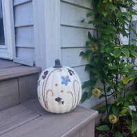 a white pumpkin with pressed flowers on a step outside next to a plant