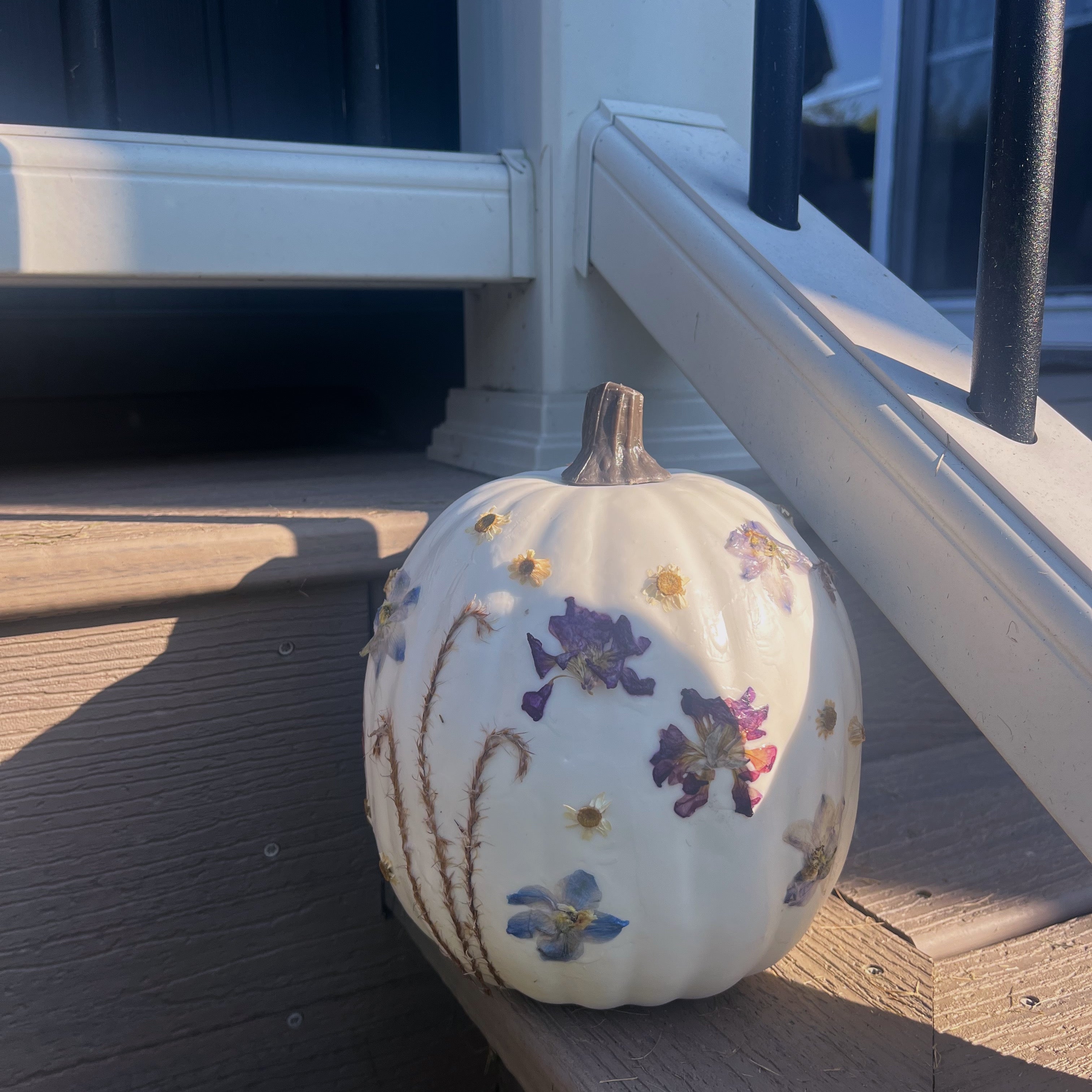 pressed flowers attached to a white pumpkin on the side of the stairs outside a house