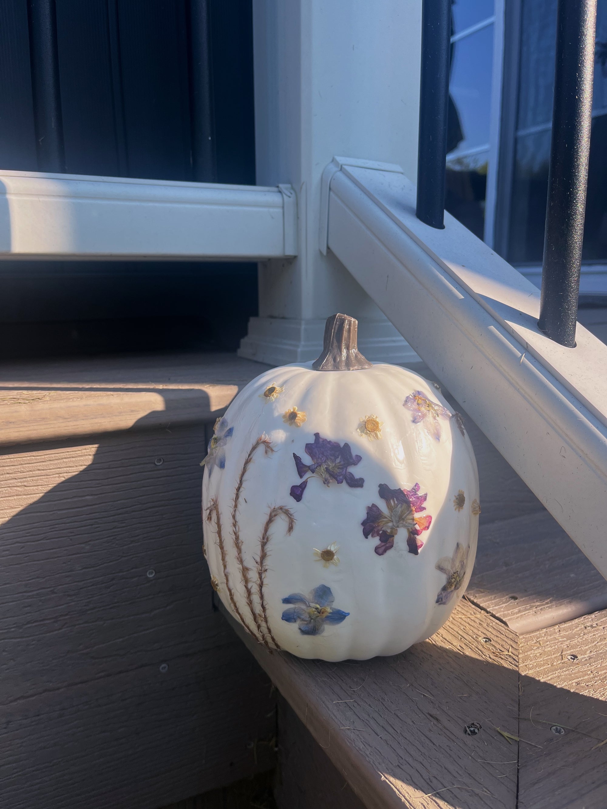 pressed flowers attached to a white pumpkin on the side of the stairs outside a house