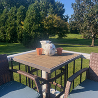 an outdoor porch with chairs and a table that has a white pumpkin with colorful pressed flowers on it and other decor with trees in the background