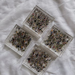 Four dried petal confetti square resin coasters include a colorful mix of flower petals, arranged in a diamond shape on a white surface. 