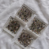 Four dried petal confetti square resin coasters include a colorful mix of flower petals, arranged in a diamond shape on a white surface. 