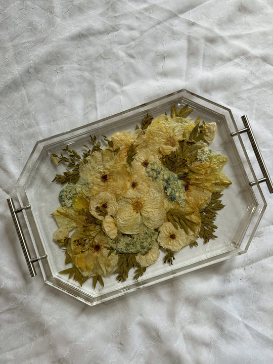 A geometric resin serving tray with silver handles features a pressed white and green bouquet, and a few blue flowers. 