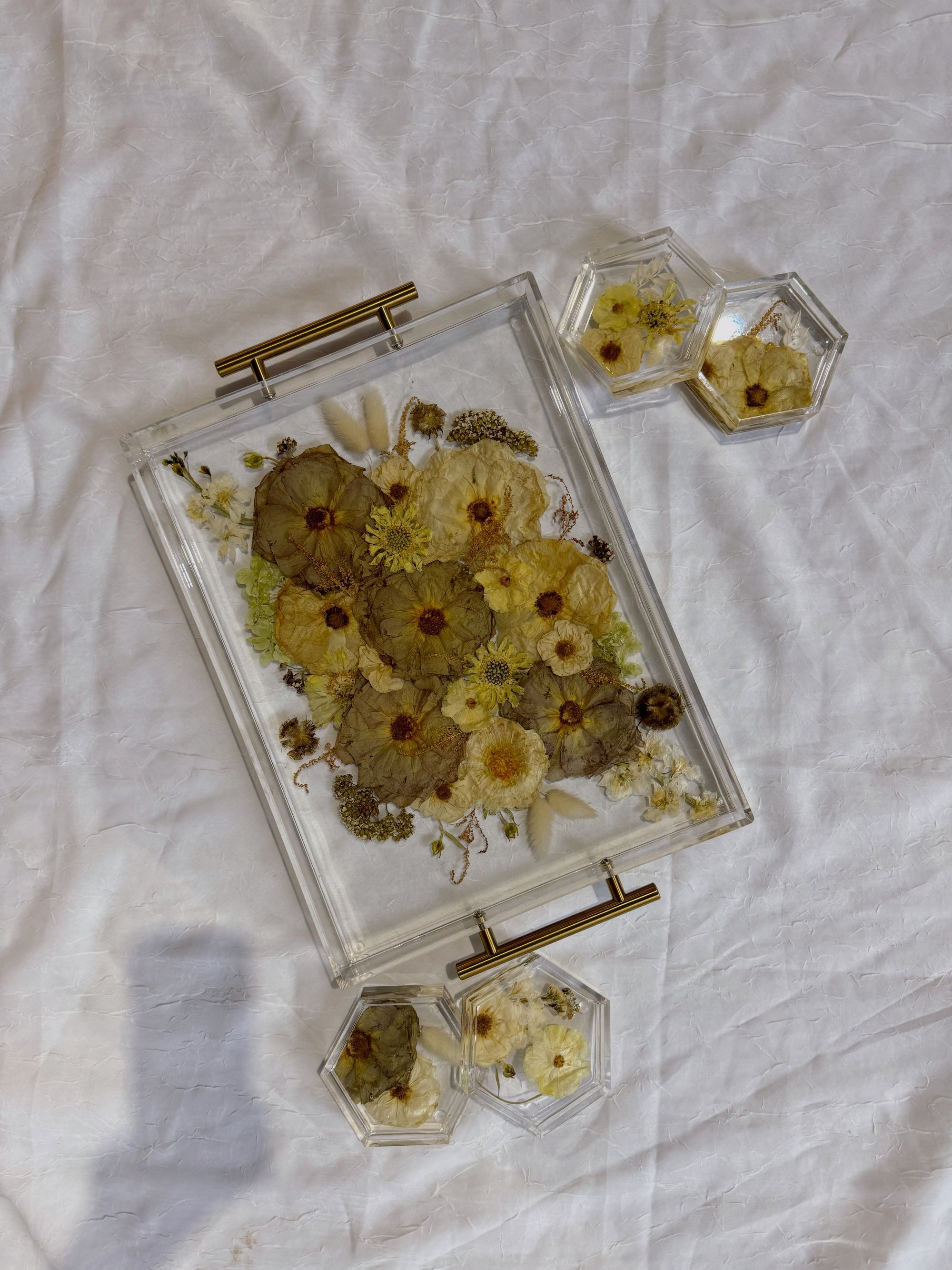 A white, pink, and green pressed bouquet is preserved in a rectangle resin serving tray with gold handles, and in four resin hexagon coasters. 