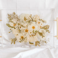 A white and green wedding bouquet pressed and preserved in a serving tray with gold handles. 